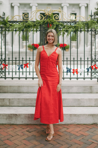 Woman wearing a sleeveless linen midi dress with gathered straps, tie-front neckline, and soft pleating, styled for a timeless and polished look.