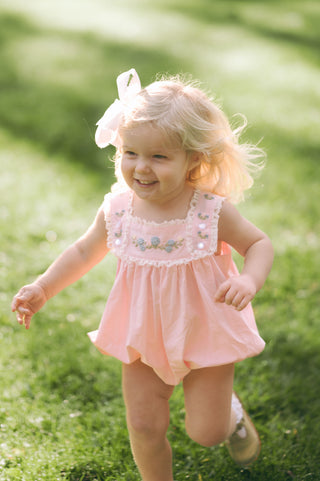 Classic heirloom baby bubble made from pale pink soft woven cotton, featuring hand-embroidered hydrangeas, delicate lace trim, and bottom snap closures.