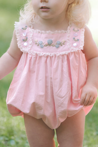 Classic heirloom baby bubble made from pale pink soft woven cotton, featuring hand-embroidered hydrangeas, delicate lace trim, and bottom snap closures.
