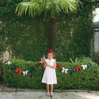 White heirloom girl’s dress with embroidered ginger jar, American flags, and floral detail; flutter sleeves and lace trim.