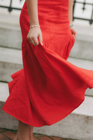 Woman wearing a sleeveless linen midi dress with gathered straps, tie-front neckline, and soft pleating, styled for a timeless and polished look.